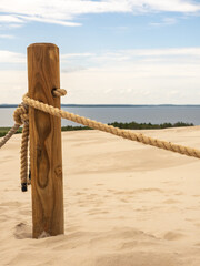 Wooden Post With Rope Barrier on Sand Dunes by the Sea Under Blue Sky and Clouds
