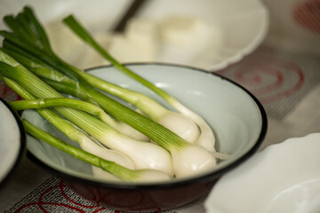 A close-up shot of freshly washed spring onions (green onions or scallions) placed in a white...