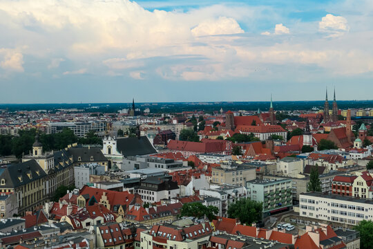 Historic churches and colorful rooftops fill the cityscape of Wroclaw, Poland, as the bustling urban environment blends tradition and modernity under a vast, cloud-streaked sky.