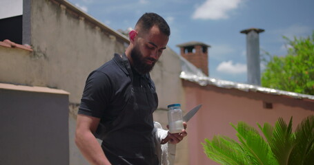 Close-up of man grilling sausages and steaks at a backyard BBQ, skillfully handling a knife and...