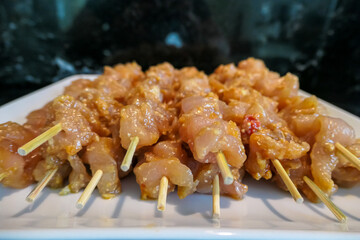 Marinated raw chicken satay skewers are neatly arranged on a white plate, prepped and ready for grilling at a barbecue, showcasing delicious and flavorful homemade appetizers or a main course.