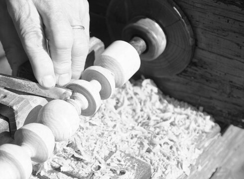 artisan hand working wooden piece with antique lathe and chisel in black and white effect
