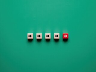 A single red block with an arrow stands out from the crowd of wooden cubes, symbolizing innovation, leadership, and taking a different approach