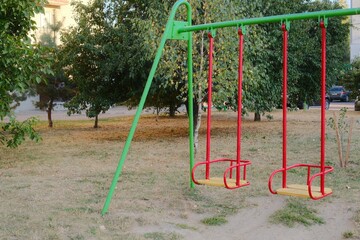 Fototapeta premium Two swings hang still in a public park setting during daytime.