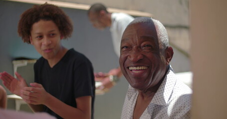 African American senior smiling brightly while enjoying a family meal outdoors, capturing joy, connection, and togetherness in a vibrant multigenerational gathering
