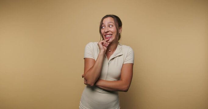footage of young woman poses playfully with a thoughtful expression, showcasing a light-hearted approach on beige background