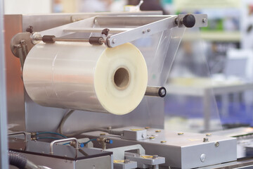 A machine with a large roll of plastic packaging film in a factory