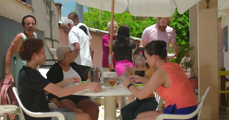 Family and friends gathered at a backyard lunch, people seated and standing, lively conversations...