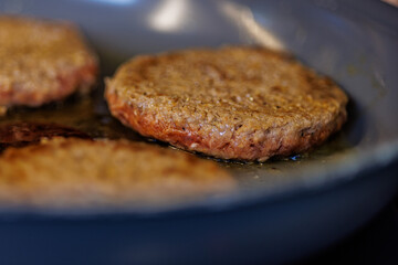 Juicy burger patties sizzling in hot oil on a dark pan, creating a mouthwatering culinary scene