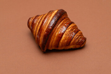 Glossy butter croissant on a warm brown background