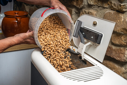 Close-up of a man filling biomass boiler or stove with wood pellets for home heating. - Powered by Adobe