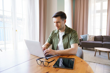 Fototapeta premium Young man works on laptop in cozy living room environment
