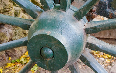Close-up of antique green wooden cart wheel with rustic details and autumn leaves scattered on the ground