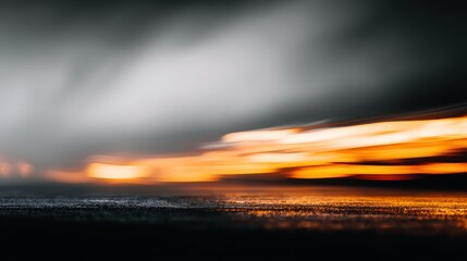 Blurred abstract landscape displays dynamic streaks of orange and yellow light blending across a dark, textured plane, beneath a cloudy, gradient sky, creating a captivating and evocative scene of...