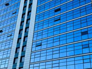 Urban abstract windowed wall of office building. Detail shot of modern business building in city. The blue reflection of the sky in the windows of the modern business center. Reflections in building. 