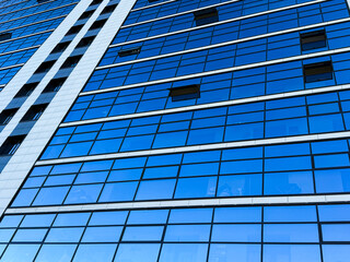 Urban abstract windowed wall of office building. Detail shot of modern business building in city. The blue reflection of the sky in the windows of the modern business center. Reflections in building. 