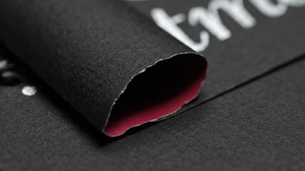 Close-up of Rolled Black Paper with White Lettering and Red Interior. - Powered by Adobe