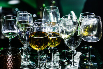 Vários copos com sobras de bebidas, acumulados no balcão do bar em uma festa, com baixa iluminação.