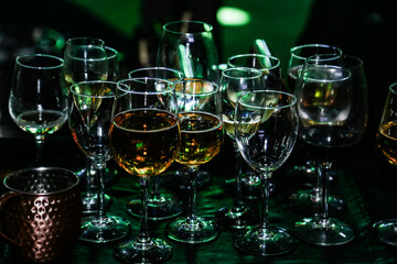 Vários copos com sobras de bebidas, acumulados no balcão do bar em uma festa, com baixa iluminação.