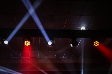 Fachos de holofotes e luzes brancas e vermelhas, em um ambiente de festa. © Angela