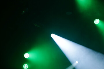 Foto de conjunto de luzes de palco, com fachos de luzes nas cores verde e branca. Desfocadas para fundo. © Angela