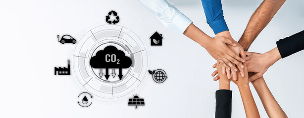 A dynamic team of diverse individuals collaborates with hands together over a backdrop of environmental icons, promoting the ideals of sustainability and teamwork in carbon reduction efforts. Trope