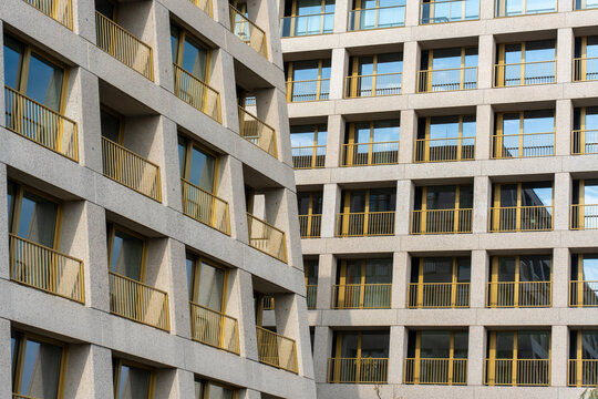 Modern residential apartment building facade with golden yellow balcony railings and geometric concrete architecture pattern. Concept for contemporary housing, urban development. 