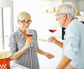 Portrait of happy senior woman holding wine glass and prepering meal in kitchen