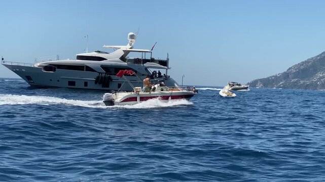 Speedboats and luxury yachts waving on water surface enjoying picturesque view of mountain cliffs along Amalfi coast, famous Amalfi, Positano, Salerno, Atrani and Praiano towns being tourist