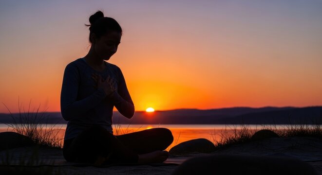 Serene woman silhouette meditating at peaceful golden hour sunset by tranquil water, expressing profound gratitude, thankfulness and inner peace with hands on heart. - Powered by Adobe