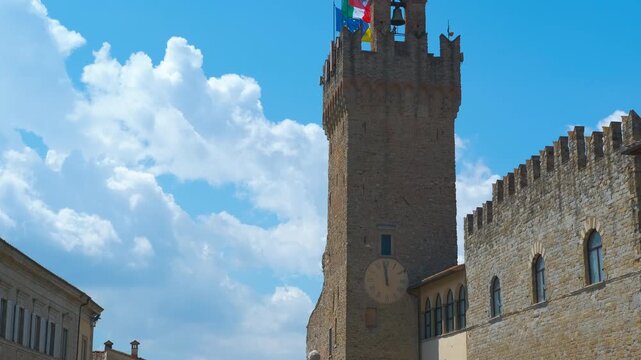 Palazzo pretorio tower with flags waving in the wind in arezzo. Palazzo pretorio tower stands tall against a blue sky, its flags fluttering gently in the breeze, showcasing the rich architectural
