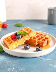 Two waffles topped with berries and mint, on a white plate