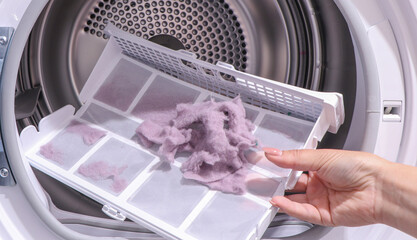 close up female hand taking lint out from dirty air filter of dryer machine after drying. cleaning Dirty filter. hair, wool from the filter in hand. Front Load Tumble Laundry electric Dryer Machine.