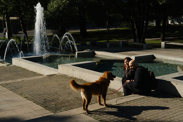 Couple with Nova Scotia Duck Tolling Retriever sitting near water fountain in Belgrade city park.