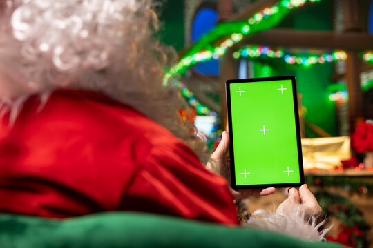 Santa Claus reads mockup tablet display to check naughty and nice kids list. Entertainer playing xmas character analyzes children behavior, preparing gifts for good children using green screen device