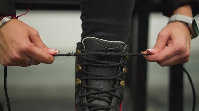 Lady tightening laces of red black ice skates closeup, hands pulling strings firmly with focus on preparation, detail of sport gear, determination, fitness, lifestyle, winter activity, performance