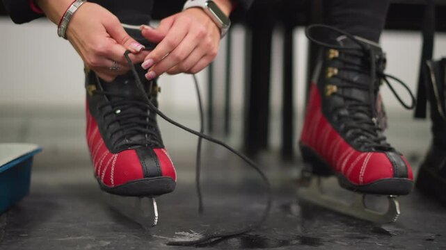 Lady putting on red black ice skates pulling laces tight on blades while preparing for skating session indoors showing hands close up with detailed focus on equipment training winter sport lifestyle