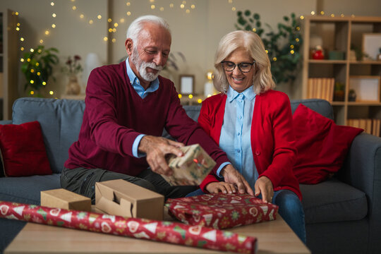 Senior couple wrapping christmas gifts together at home
