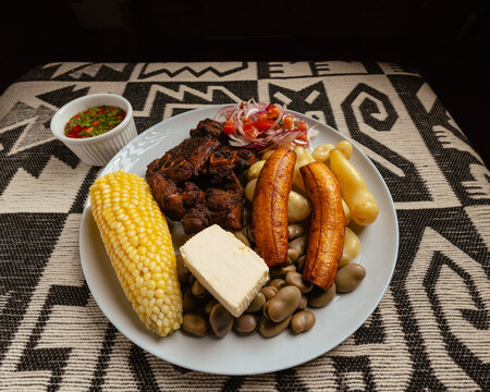 Traditional dish of fritada made with pork and served with corn, beans, cheese, fried banana, fresh salad, and Hot sauce.