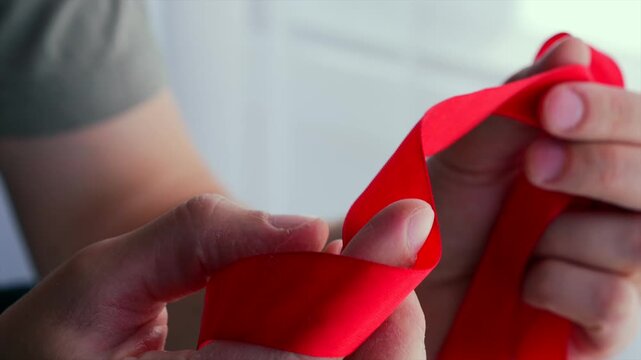 A long red ribbon in the hands of a seamstress.
Fabric and textile processing.
A red silk ribbon unrolled in a person's hands.
Ribbon, long, bandage, roll