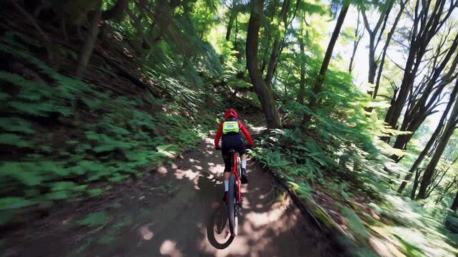 Mountain biker wearing a red and yellow jacket riding a bicycle on a winding dirt path, surrounded by dense green foliage and trees with motion blur conveying speed and dynamism