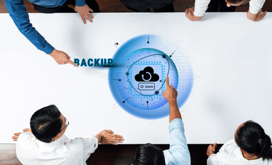 A top-down view of business professionals discussing cloud backup solutions with digital visuals,...