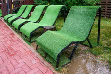 Outdoor benches, deck chairs covered with decorative green grass on the street on a rainy day. An outdoor eco-friendly place to relax