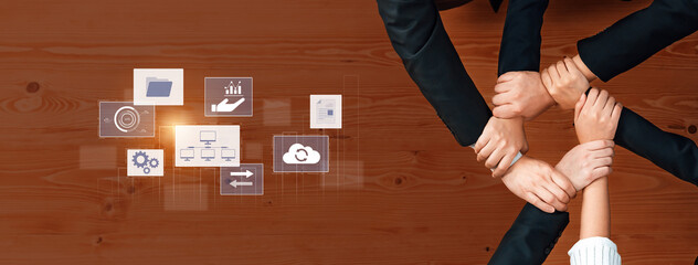 Hands join together in a display of teamwork and collaboration over a wooden table. Digital icons reflect various business ideas, emphasizing synergy and creativity while strategizing. Trope