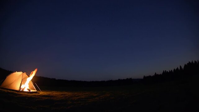 Illuminated tent and burning campfire creating a warm glow in a dark natural landscape, representing outdoor adventure, relaxation, and an escape into nature under the night sky - Powered by Adobe