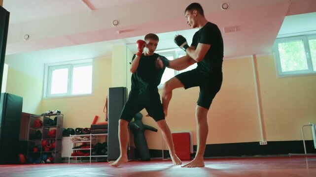 Two wrestlers sparring in gym on red mat, facing each other in combat stance, wearing gloves, barefoot, practicing martial arts with focus on strength, endurance, discipline, fighting technique