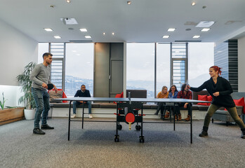 Fototapeta premium Business colleagues take a break from work to enjoy a game of table tennis, fostering teamwork and camaraderie in the workplace