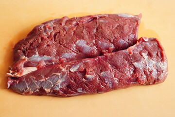 Fresh raw venison meat block on a wooden cutting board, close-up of wild game red meat with texture details for cooking or gourmet ingredient concept
