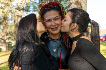 Two young women kissing their happy mother on both cheeks outdoors showing love and affection