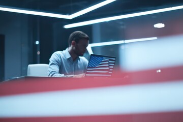 Professional working in a modern office setting with a laptop displaying the USA flag during late evening hours in a well-lit environment